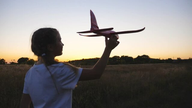Cute small girl plays with plane while walking on country trail at dusk time. Carefree little kid going with toy and launching airplane outdoor. Pretty child enjoying stroll at nature. Childhood dream