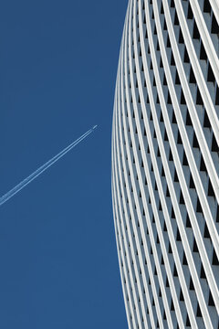 Detail of a skyscraper against a clear blue sky with an airplane trace.