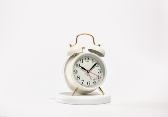 A white vintage retro alarm clock stands on a round white stand. Morning preparation for work or school.