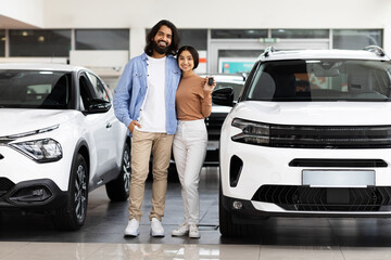 Smiling millennial indian couple standing next to new car