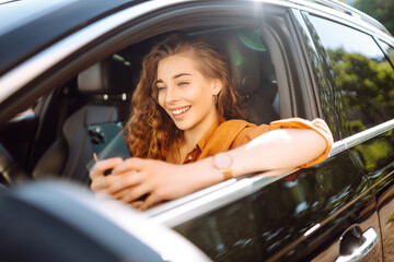 Woman driver in a car with a phone in her hands. Beautiful woman texting on a cell phone and waiting in the city traffic. Leisure, travel, technology, navigation.