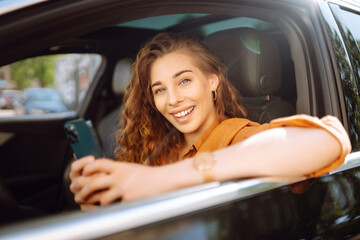 Woman driver in a car with a phone in her hands. Beautiful woman texting on a cell phone and waiting in the city traffic. Leisure, travel, technology, navigation.