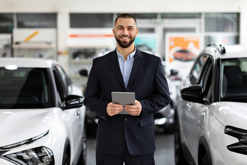 Car seller standing in auto salon and using tablet