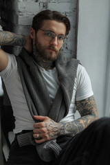 Stylish handsome young hipster man with tattoo with hairstyle and beard with fashion glasses in a...