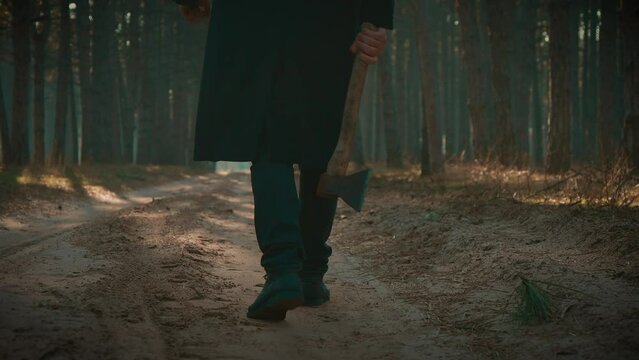 Serial killer with axe wants to commit murder in woods, unrecognizable murderer walking through woods, view on feet. Mentally ill depressed male, angry maniac