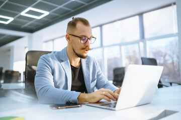Young man wearing glasses working with laptop while sitting at his working place. Business, technology, study.