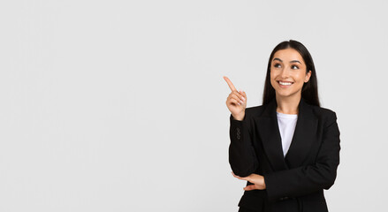 Cheerful businesswoman pointing upwards at free space and smiling