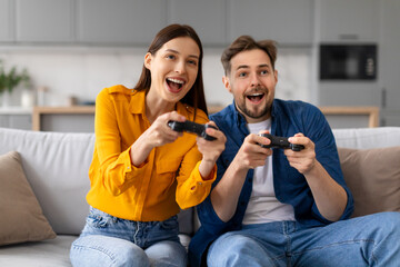 Excited young couple playing video games together on couch