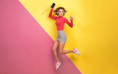 smiling attractive smiling excited woman in stylish colorful outfit jumping and listening to music
