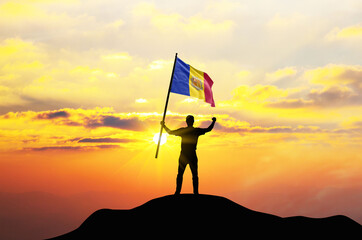 Andorra flag being waved by a man celebrating success at the top of a mountain against sunset or sunrise. Andorra flag for Independence Day.