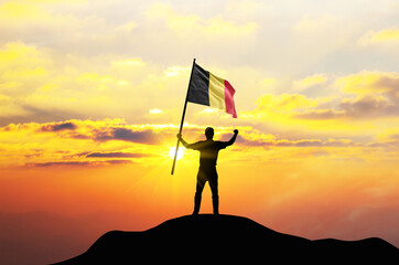 Belgium flag being waved by a man celebrating success at the top of a mountain against sunset or...