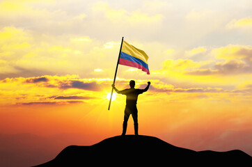 Colombia flag being waved by a man celebrating success at the top of a mountain against sunset or sunrise. Colombia flag for Independence Day.
