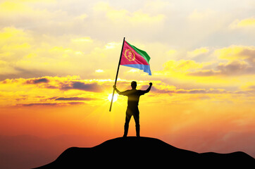 Eritrea flag being waved by a man celebrating success at the top of a mountain against sunset or sunrise. Eritrea flag for Independence Day. - Powered by Adobe