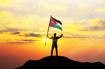 Jordan flag being waved by a man celebrating success at the top of a mountain against sunset or sunrise. Jordan flag for Independence Day.