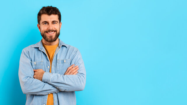 Happy millennial guy confidently stands with arms crossed in studio