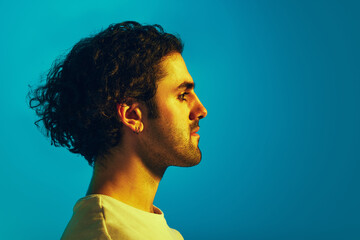 Side view portrait of young man with curly dark hair and unshaved face looking straight against...