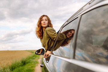 Young woman leaning out of the car window enjoying nature. Girl is resting and enjoying journey....