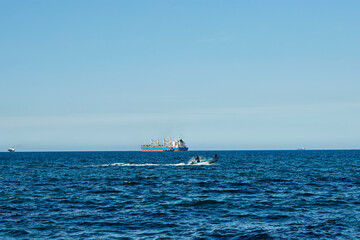 Fototapeta premium Mascara, Sig - Algeria - February 13 2024: a view of large container cargo and fishing boat on tranquil, sunny blue ocean