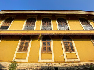 Exterior facade of an old Portuguese era house with yellow walls and rectangular windows in the town of Margao in Goa.