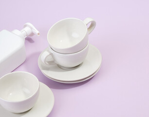 Set of clean washed dishes and cups on a purple background. The white detergent dispenser is on the table.
