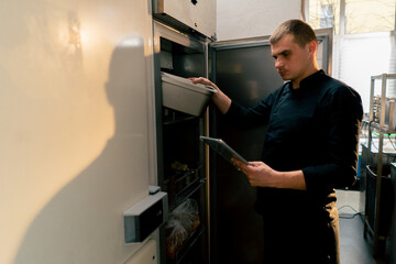 chef stands in a professional kitchen in a black uniform and looks through what is on the list in...