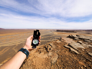 Hand holding compass with Morocco desert in the background, concept of adventure and freedom.