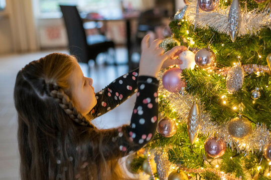 Single mum helping her daughters place ornaments on their tree. A beautiful bonding moment with twinkle lights and baubles.