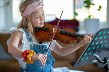 Young teenage girl playing violin, practising her new music.