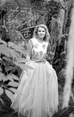 Black and white photo of a stunning girl in a wedding dress, blonde with long curls posing in nature. Women concept