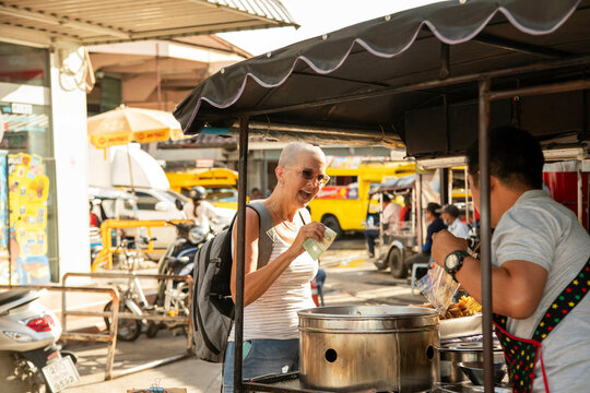 Mid aged woman solo traveller stops to buy street food from a vendor in Chiang Mai. Thailand