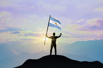 Argentina flag being waved by a man celebrating success at the top of a mountain against sunset or sunrise. Argentina flag for Independence Day.