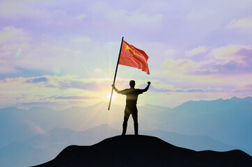 China flag being waved by a man celebrating success at the top of a mountain against sunset or...