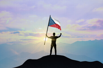 Czech Republic flag being waved by a man celebrating success at the top of a mountain against sunset or sunrise. Czech Republic flag for Independence Day.