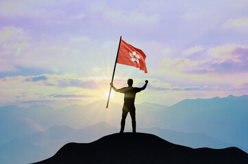 Hong Kong flag being waved by a man celebrating success at the top of a mountain against sunset or sunrise. Hong Kong flag for Independence Day.