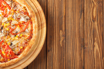 delicious pizza with chicken, mushrooms, cheese, tomatoes and corn on a wooden background