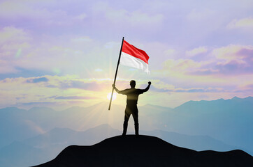 Indonesia flag being waved by a man celebrating success at the top of a mountain against sunset or sunrise. Indonesia flag for Independence Day.
