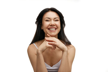 portrait of smiling woman in white tank holds head tilted and hands together against white studio background. Concept of beauty and fashion, spa treatments, self care, body care, wellness. Ad