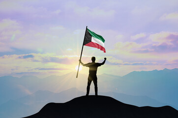 Kuwait flag being waved by a man celebrating success at the top of a mountain against sunset or sunrise. Kuwait flag for Independence Day.