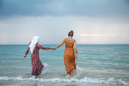 Two young women, best friends one is wearing a hijab having fun and enjoying time at the beach.