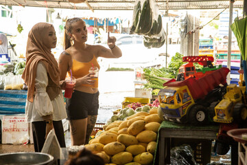 Two young women one wearing a hijab  in a fruit shop in Thailand.