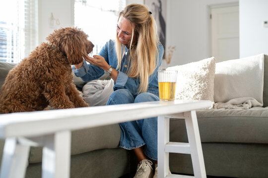 Attractive blonde woman sitting on her sofa speaking to her dog giving him affection