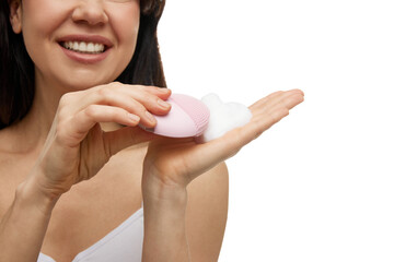 Close-up portrait of of woman holding pink facial cleansing brush with foam against white studio background. Concept of beauty and self care, wellness, skincare, hygiene procedures.