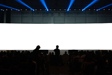 Front view of mockup on big blank white screen with space in empty huge hall with scene and silhouette of audiences