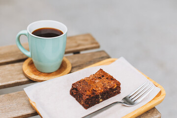 Cup of black coffee and a brownie cake on a table in a street cafe.