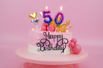 Pink birthday cake with golden crown and pink burning candles, numbers 50 on pink.	