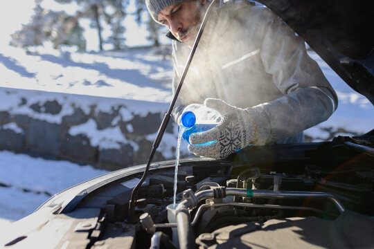 Outdoor winter scene of man pouring antifreeze windshield liquid. Car maintenance concept.