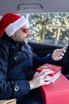 Man holding cellphone while sitting on rear seat in the car. Christmas holidays and travel concepts.