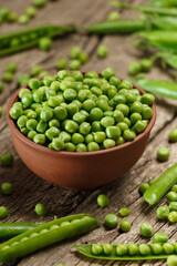 Green peas in closed and open pods, peeled peas in a bowl, scattered pea seeds on a wooden background.