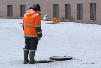 A worker in an orange uniform stands over an open sewer, Palace Square, St. Petersburg, Russia, January 16, 2024