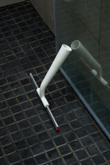 Plastic shower wiper on a shower floor with dirty lime glass door